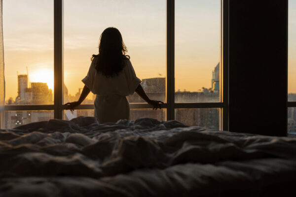 Imagen de mujer mirando la ciudad desde la ventana de su apartamento.