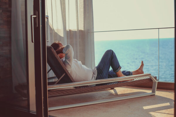 Imagen de hombre descansando en una tumbona en la terraza de su apartamento frente al mar.